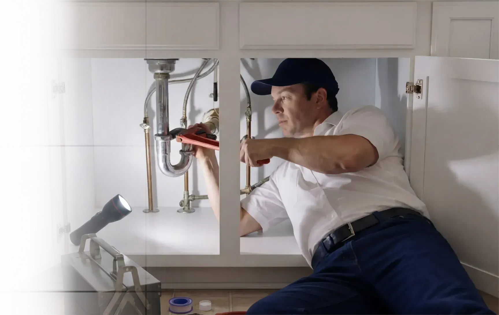 Plumber repairing pipes under a bathroom sink with a wrench